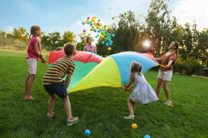 Group,of,children,and,teachers,playing,with,rainbow,playground,parachute
